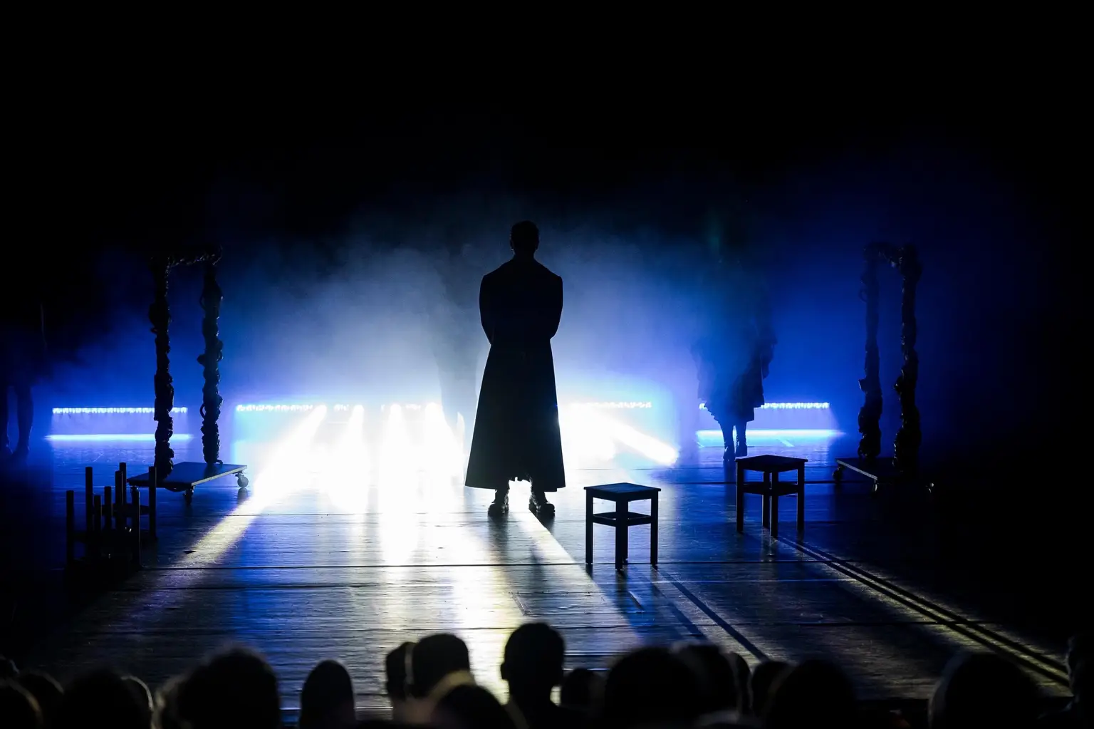 Szene aus ANTIGONE: eine Figur als Silhouette vor hellem Bühnenlicht und Nebel.